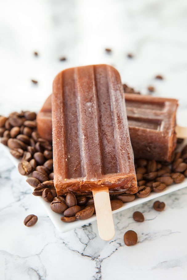 Iced coffee popsicles on a plate of coffee beans